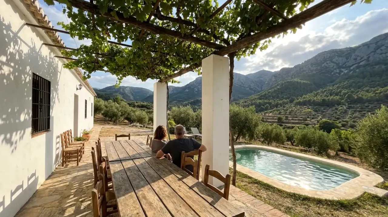 Porche del cortijo con la mesa grande bajo la parra, la piscina y la sierra al fondo