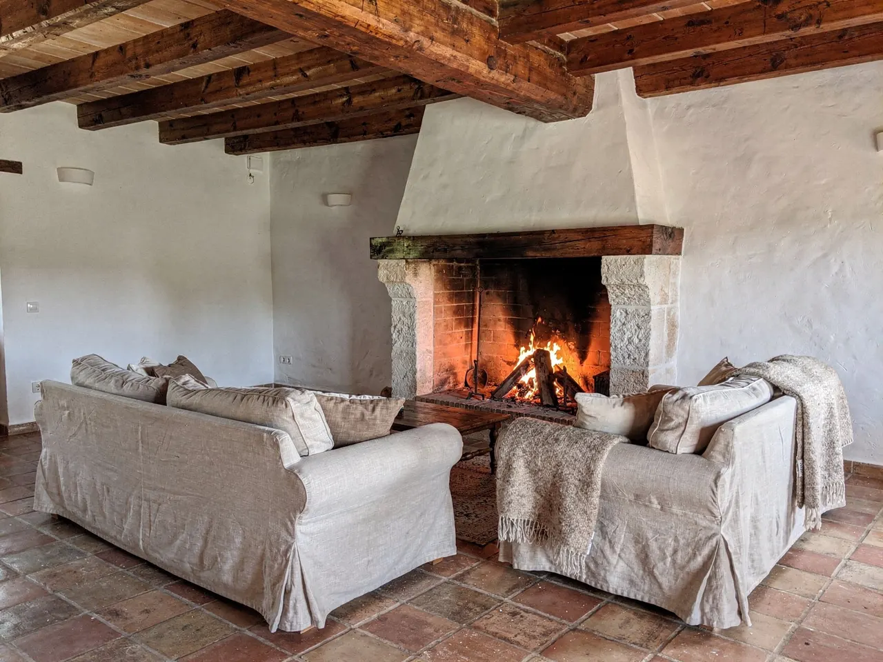 Salón con la chimenea encendida, sofás de lino y vigas de madera